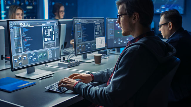 智能男性IT程序员在数据中心系统控制室中在桌面绿色模拟屏幕上工作。年轻专业人士编程的团队编程复杂的代码